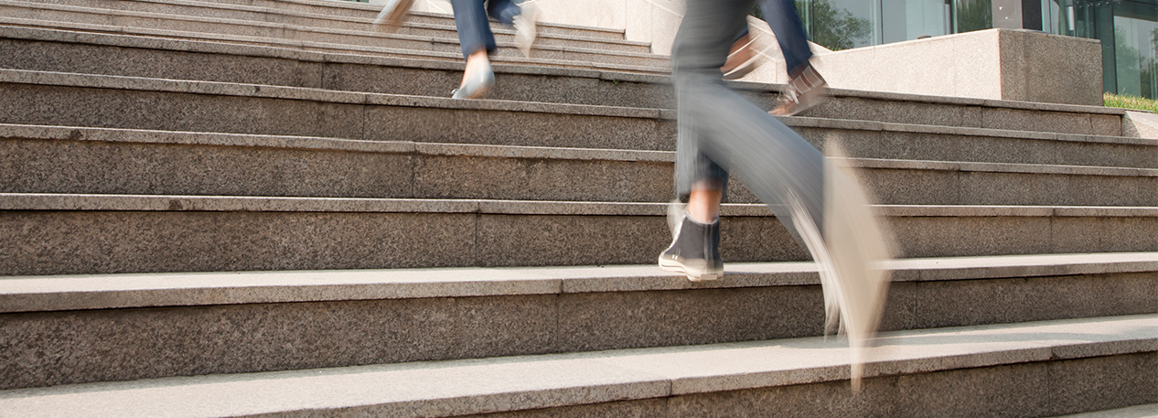 Students with backpacks running up concrete steps toward a college academic building