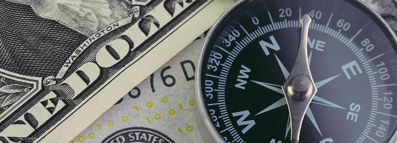 Close up shot of a compass atop of several one dollar bills