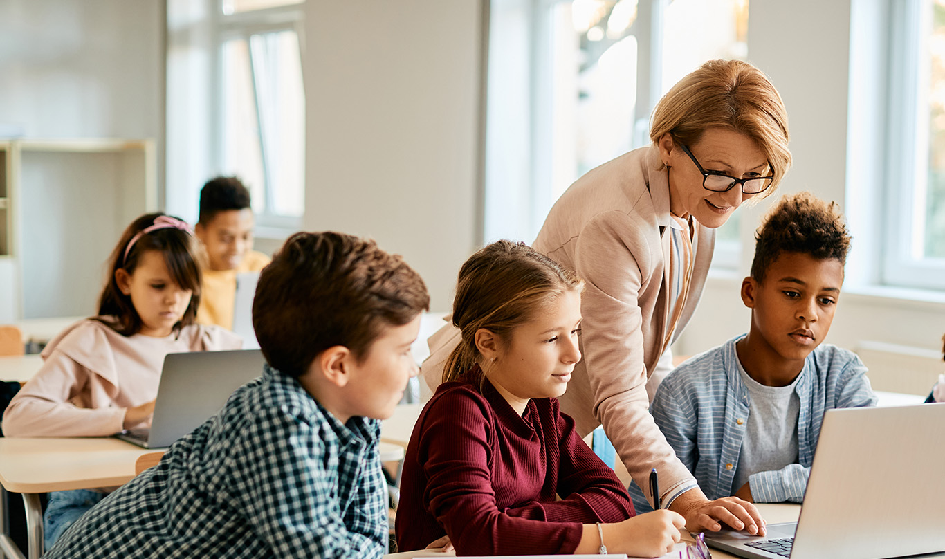 A teacher helps students at their desks.