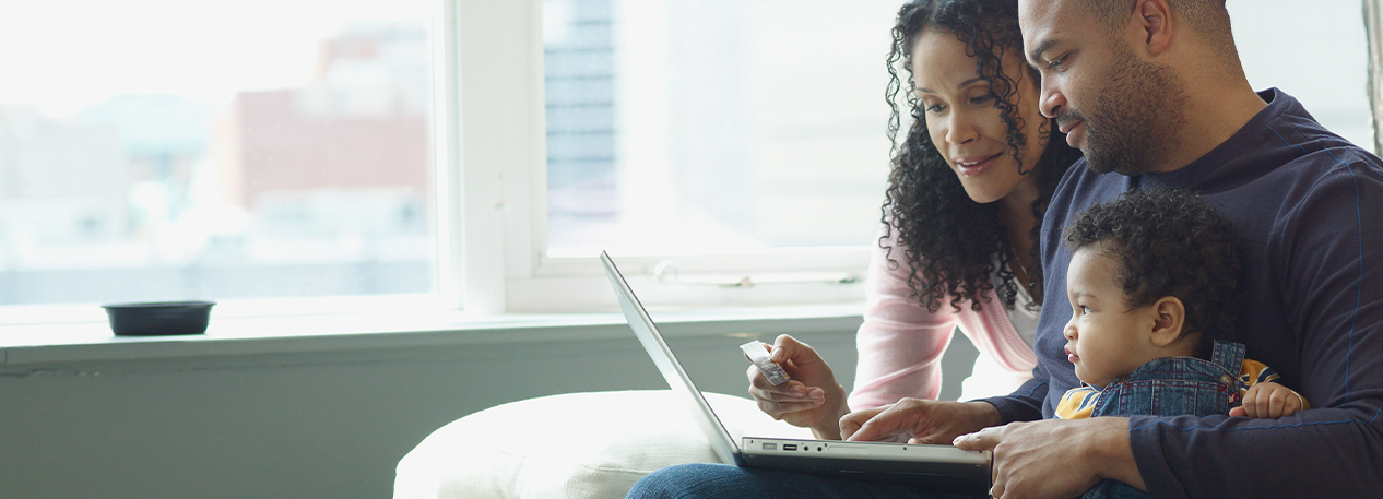 A mother and father review information on a laptop, while their young son sits on dad's lap.