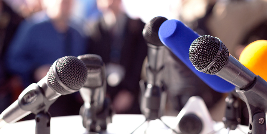 A variety of microphones sitting on a table with an audience in the distance