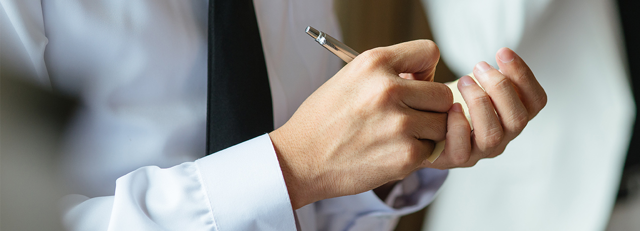 Man in a tie writing with a pen on a small notepad