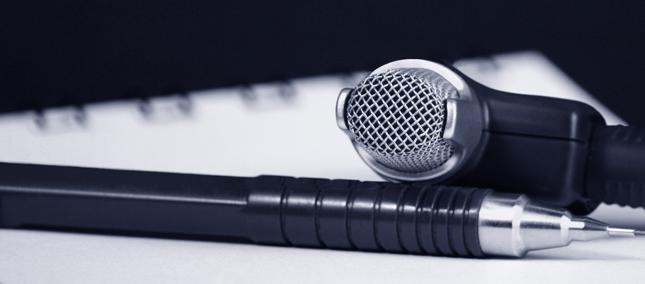 A spiral notebook with a pen and microphone sitting on top