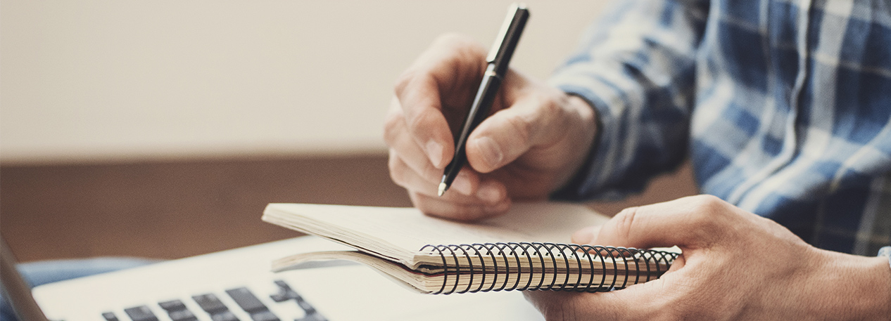 Man with a laptop computer, writing in a spiral notepad