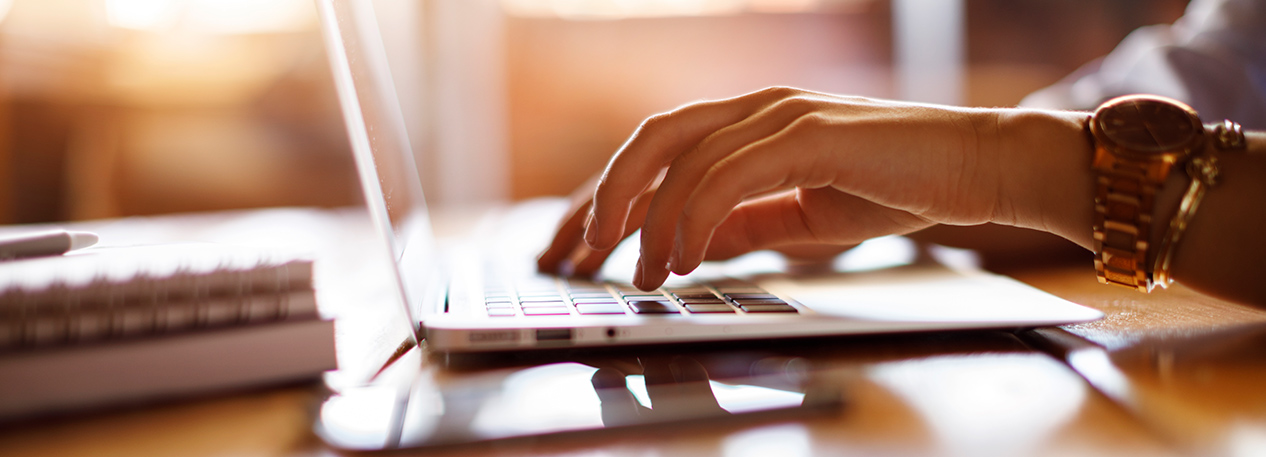 Hands typing on a laptop computer with a notepad and pen nearby