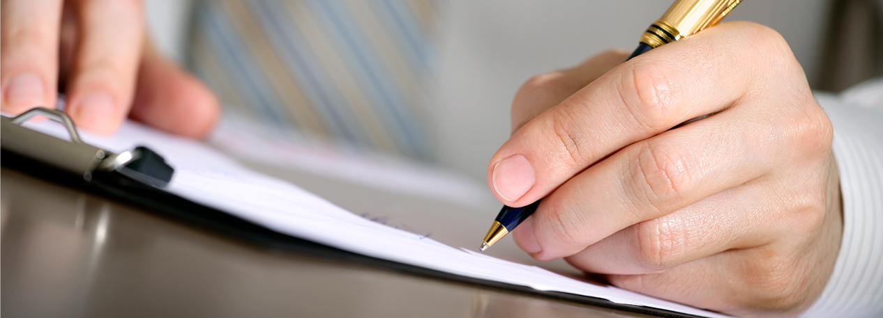 Man in a shirt and tie holding a pen and signing a document.