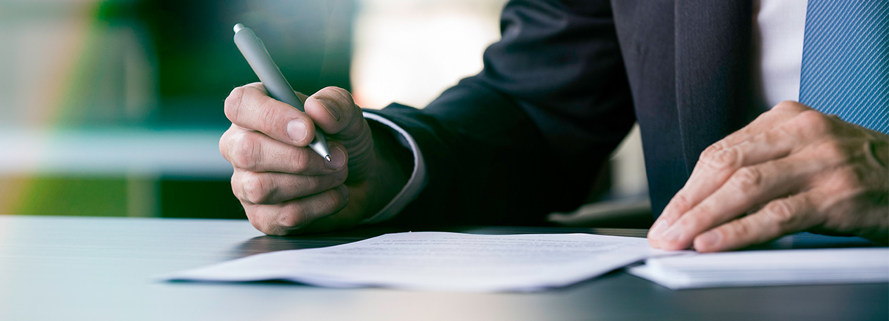 Man in a suit holding a pen and signing a document.