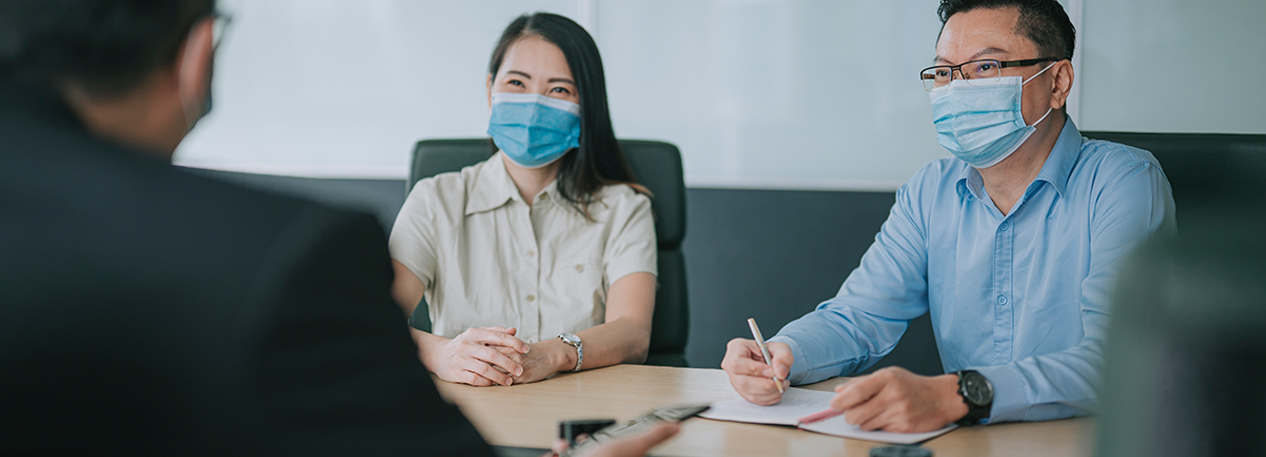 Three people wearing masks sitting around a table and signing a document.