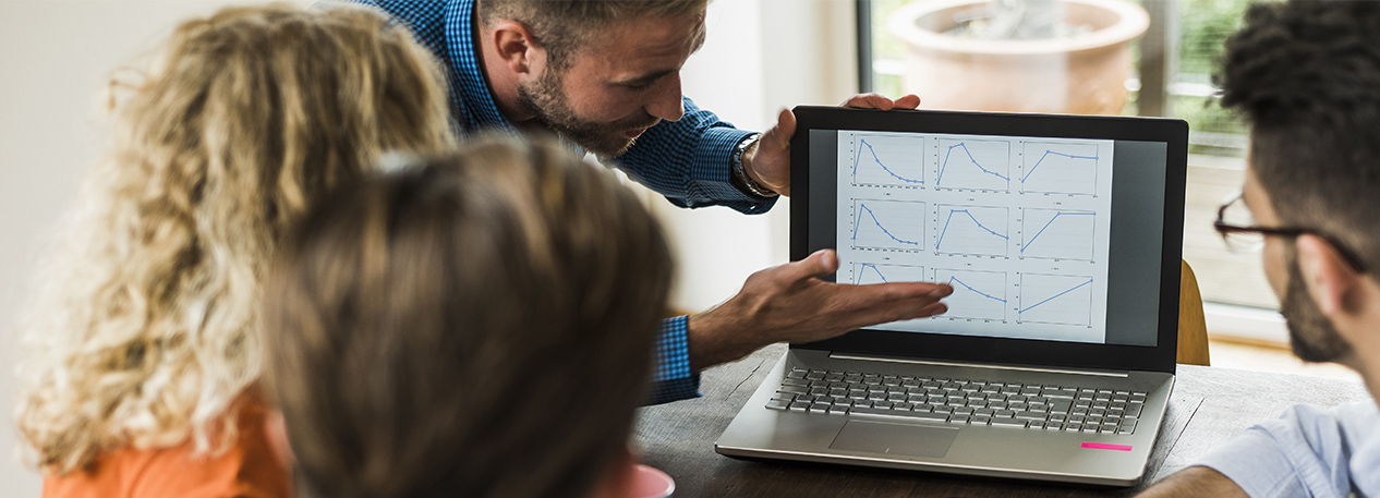 A group of colleagues review a chart on a laptop.