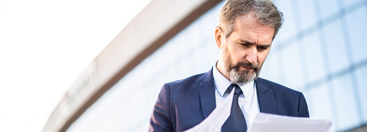 Man in a business suit standing outside a building and looking at papers.