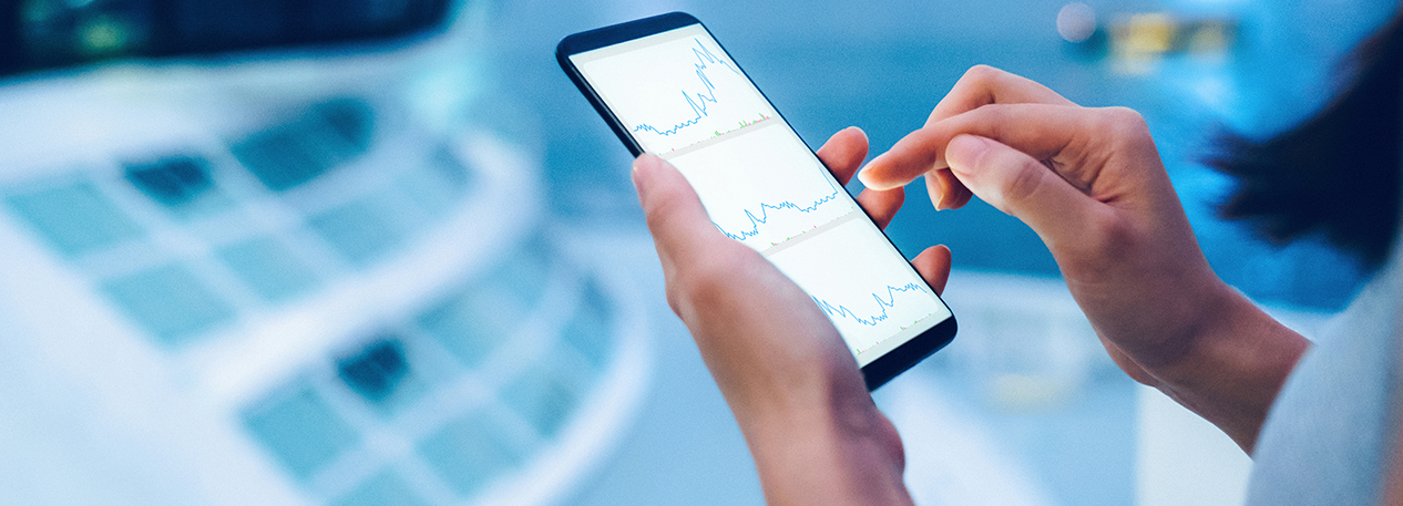 Hands holding a cell phone that shows a series of three line charts