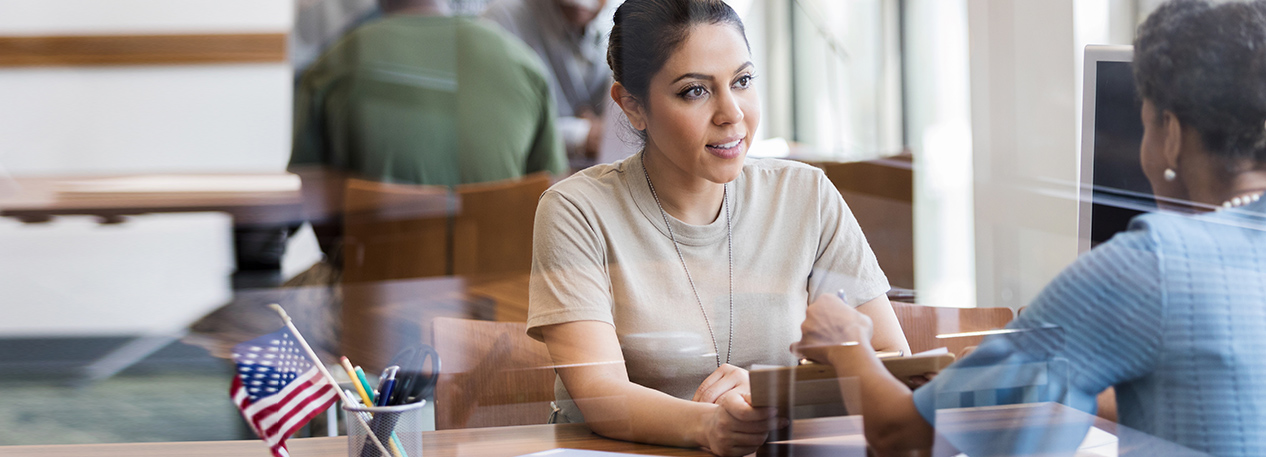 A woman meets with a female banker at a desk to discuss business matters.