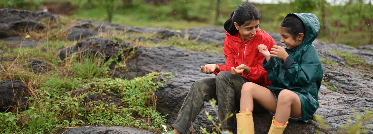 A mother and daughter sit on a rock, taking a break during their rainy day hike.