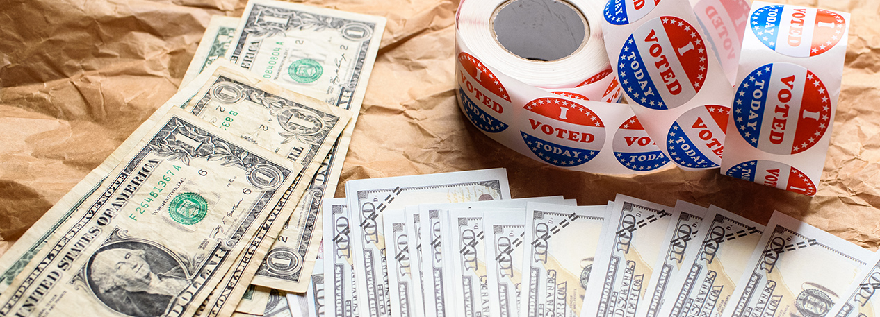 Stacks of one dollar and hundred dollar bills on a table with a roll of "I Voted" stickers.