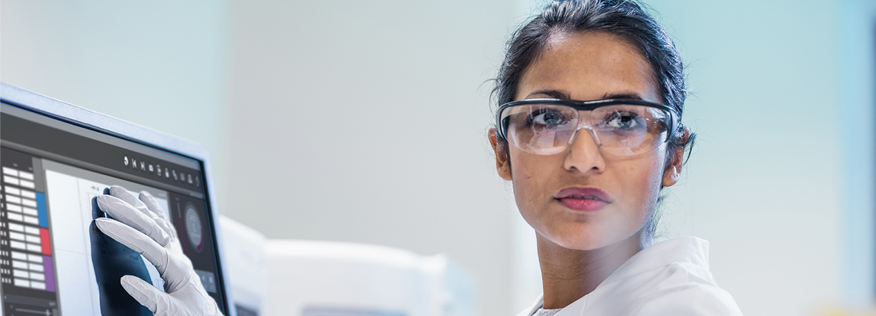 Woman in a laboratory wearing goggles and using a touch-screen device.