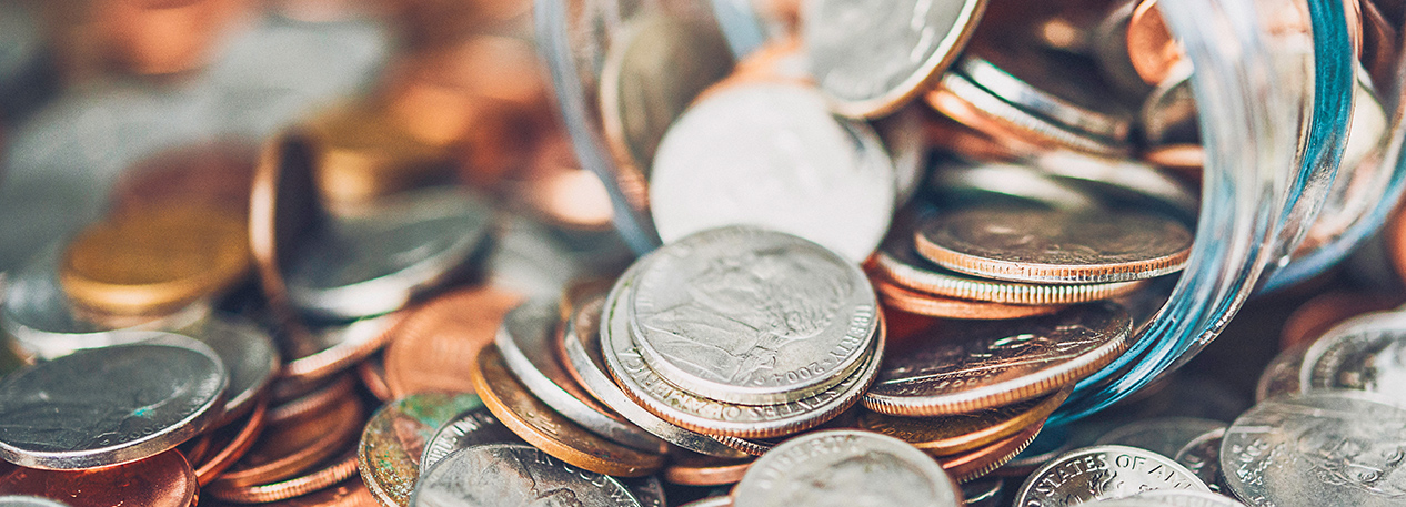 Glass jar of coins on its side, with some of the coins spilling out onto the table