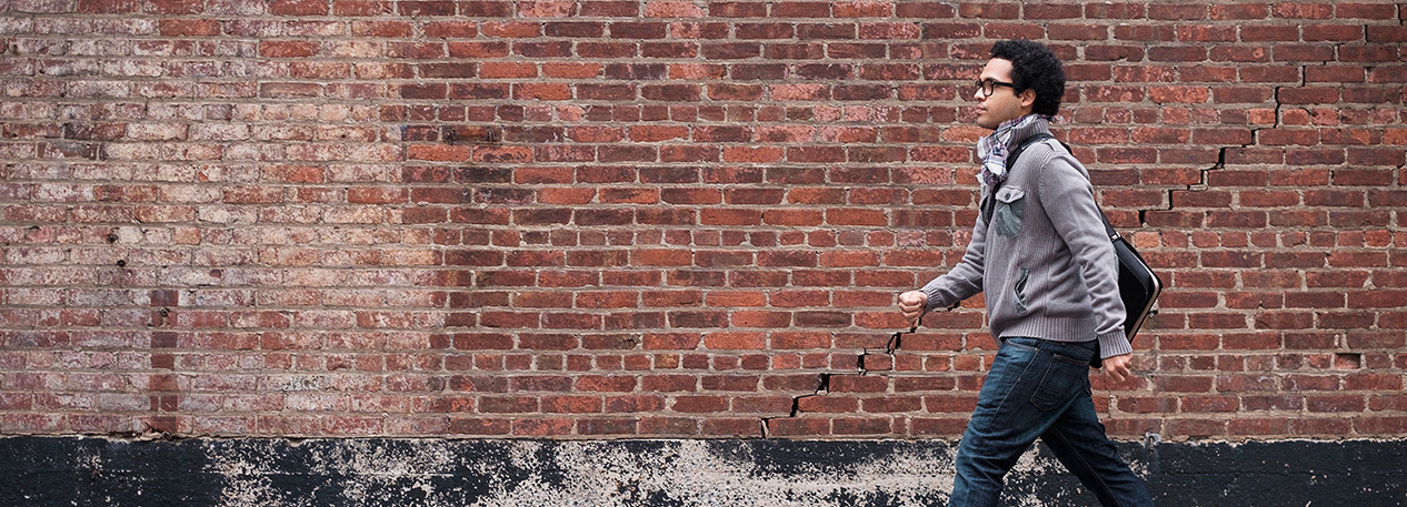A man walks briskly past a brick wall on a city street.