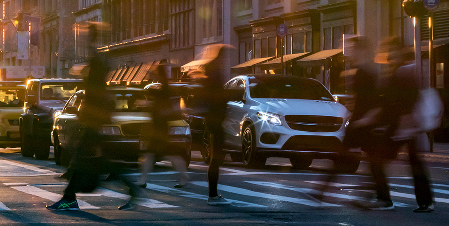 Cars stopped at a city intersection with pedestrians crossing in front of them in the crosswalk