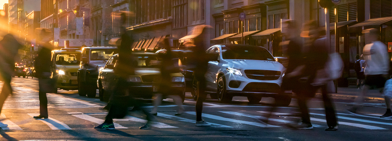 Cars stopped at a city intersection with pedestrians crossing in front of them in the crosswalk