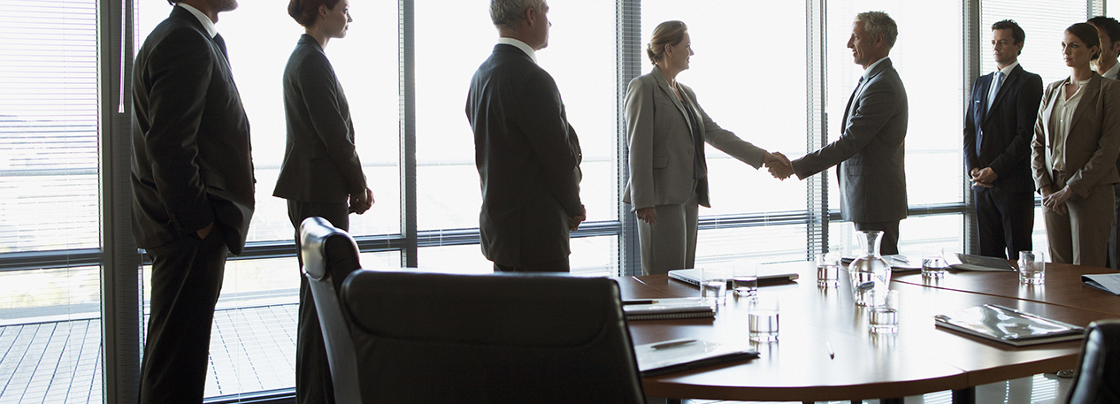 Two people in a conference room shaking hands while coworkers look on
