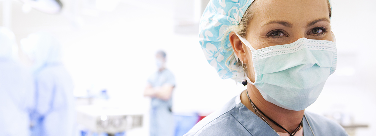 Close-up of a face of a nurse wearing a mask and scrubs in the forground of others in scrub in the blurred background