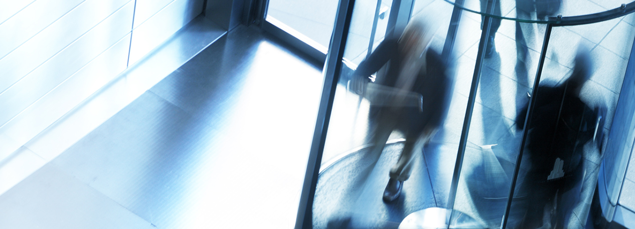 Two people walking through a revolving door.