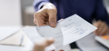 Close-up of a person handing another person a check.