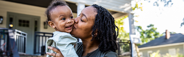 A mother kisses her infant in their front yard.