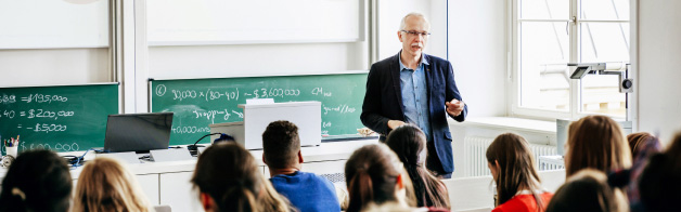 Teacher standing in front of classroom of college age students.