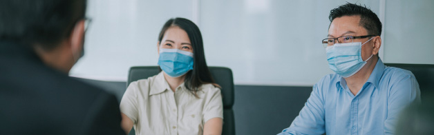 Three people wearing masks sitting around a table and looking at documents.