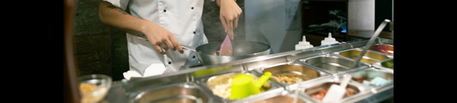 Restaurant worker in a white chef's coat cooking in a kitchen.