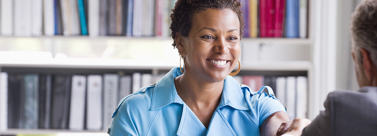 A woman dressed in blue shakes the hand of a business partner.