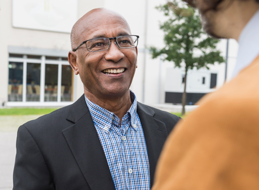 Smiling man in sport coat speaking to another person